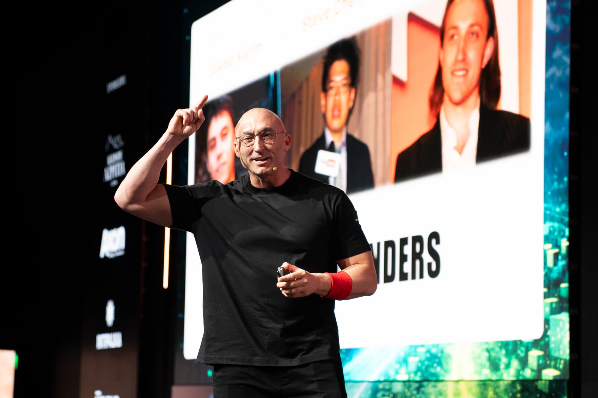 JJ Delgado on stage at a global leadership event, gesturing toward the audience.